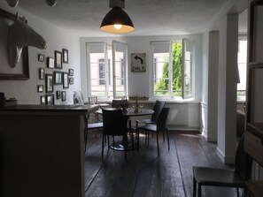 A dining area with a table and chairs, a hanging light fixture, and a window with a view of greenery.