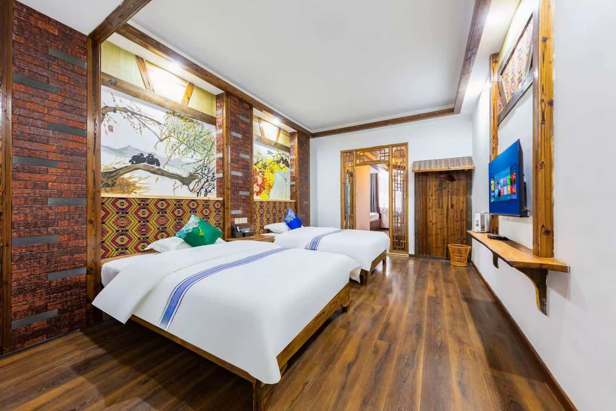 Une chambre d’hôtel avec deux lits, un plancher en bois, un mur en briques et une grande fenêtre ornée d’œuvres d’art.