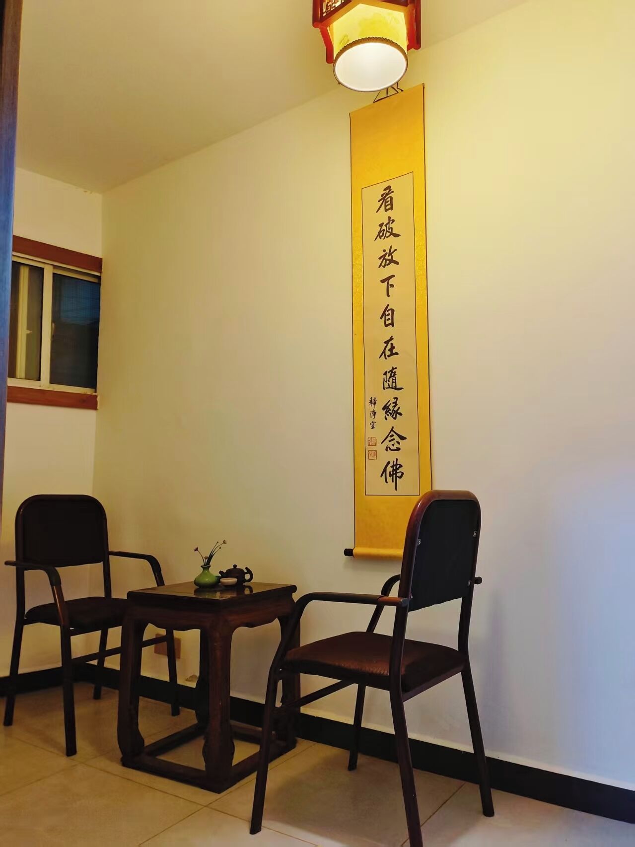 A room with a table and two chairs, a window, and a wall-mounted sign with Chinese characters.