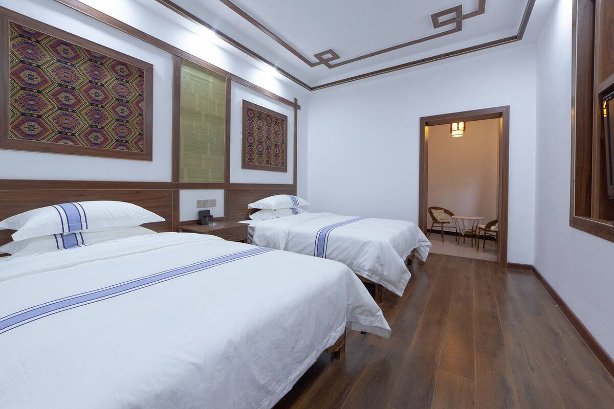 Une chambre d’hôtel avec deux lits, un plancher en bois et un petit coin salon avec une table et des chaises.