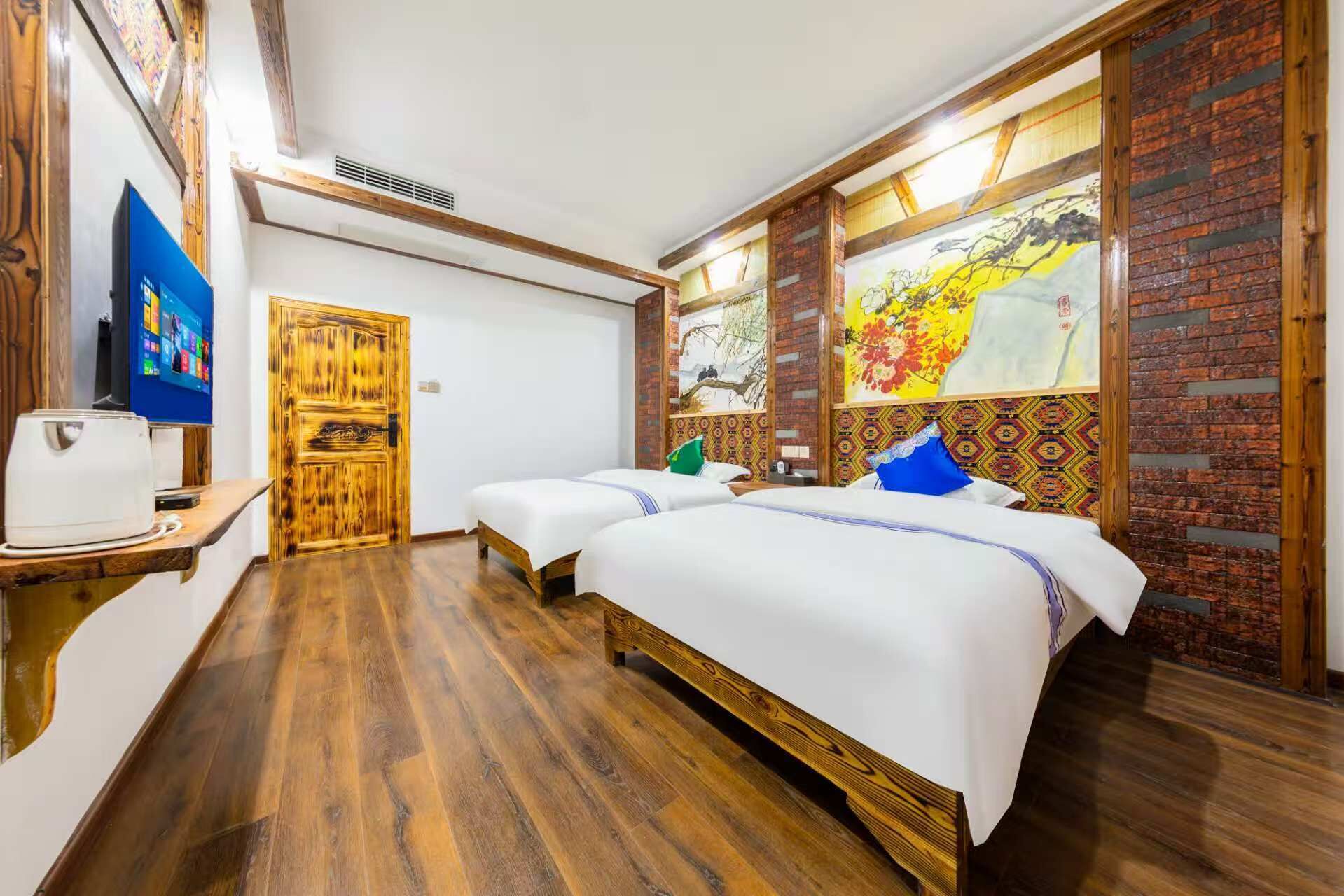 Habitación de hotel con dos camas, suelo de madera, televisor y puerta de madera.