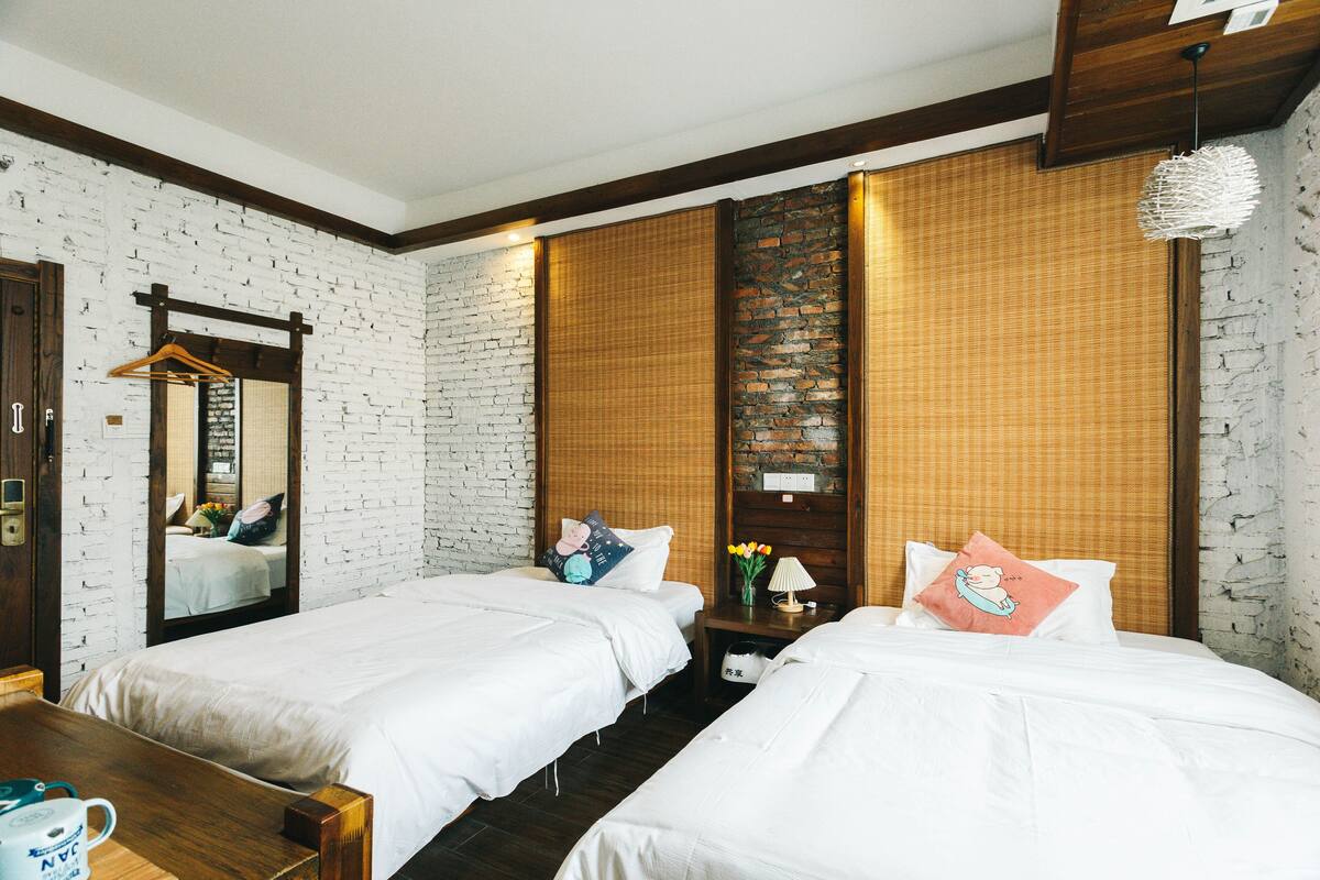 Une chambre d’hôtel avec deux lits simples, une commode en bois, un miroir et un mur avec un motif en briques.