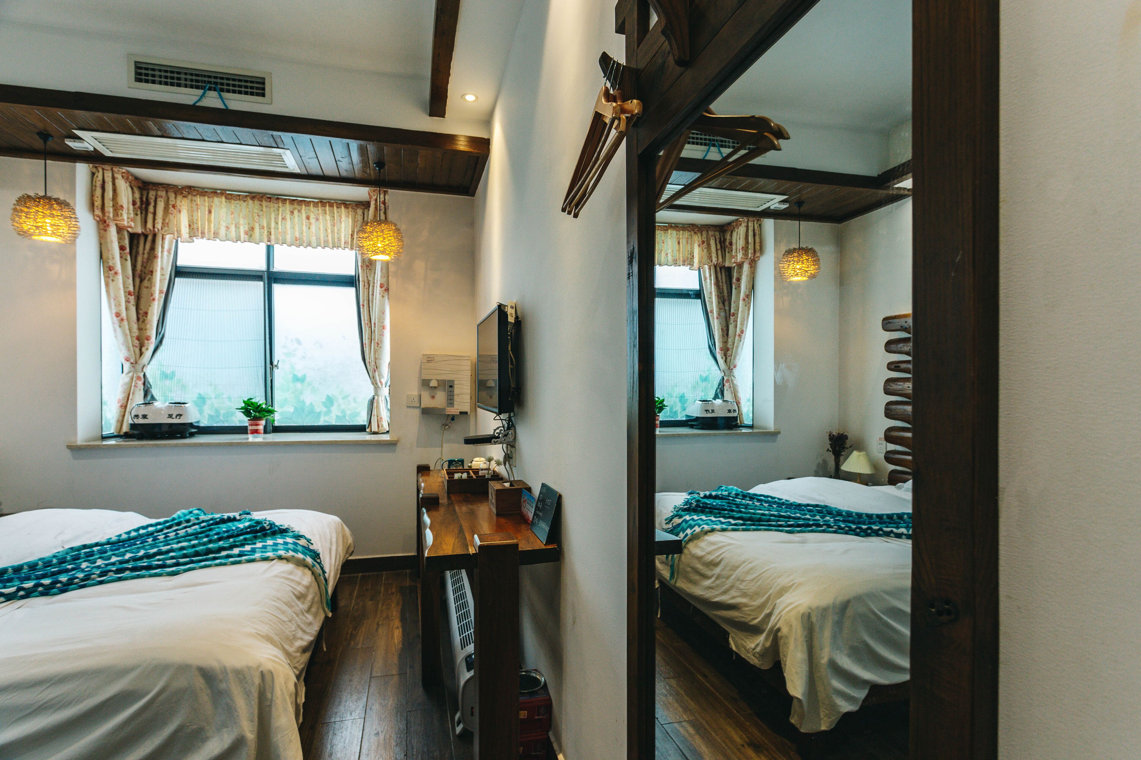 Une chambre avec deux lits, un bureau, une chaise, un miroir et une fenêtre avec des rideaux.