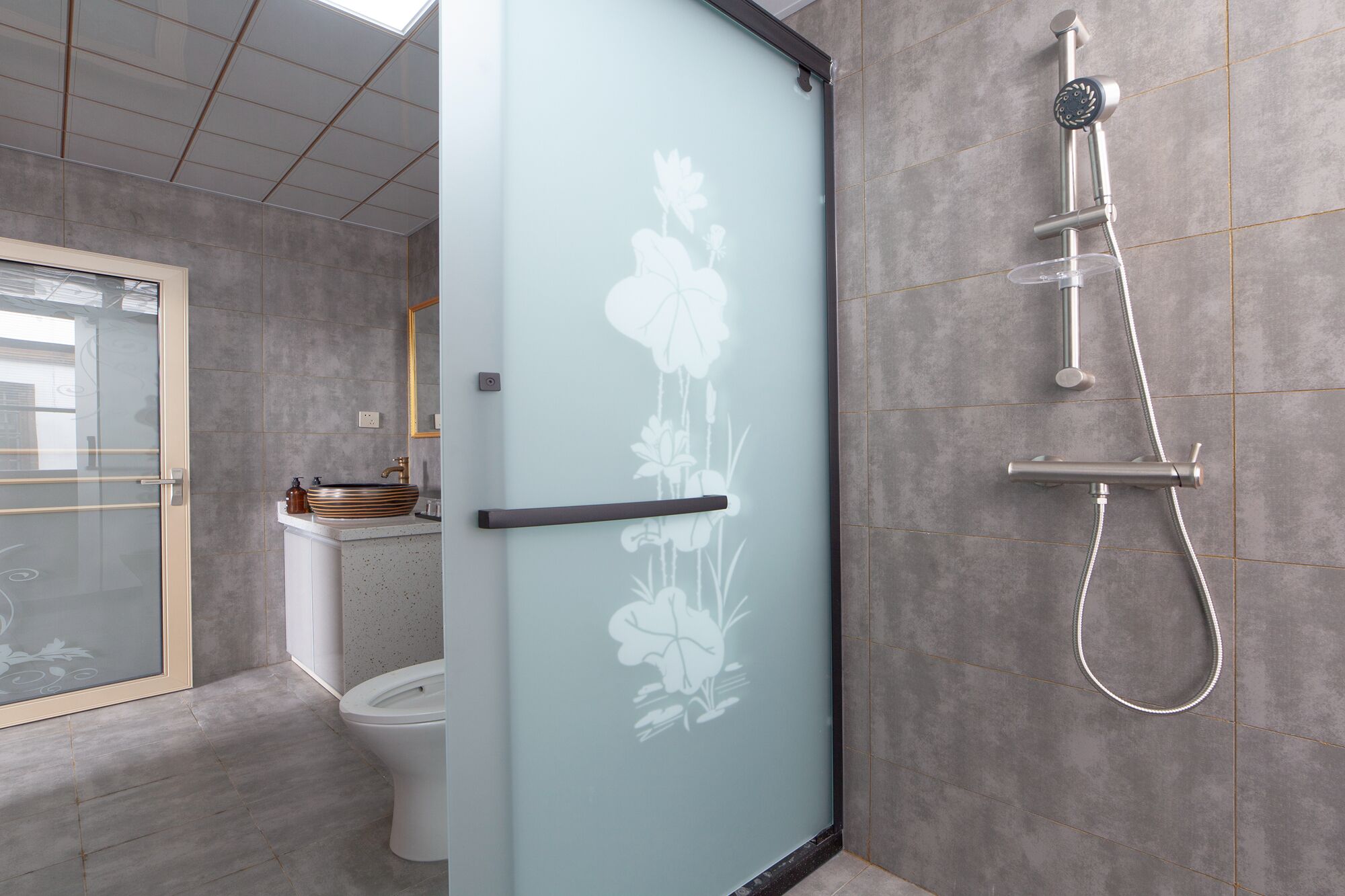 Un bagno moderno con una porta in vetro satinato, un water, un lavandino con una bacinella a righe e una doccia con soffione manuale.
