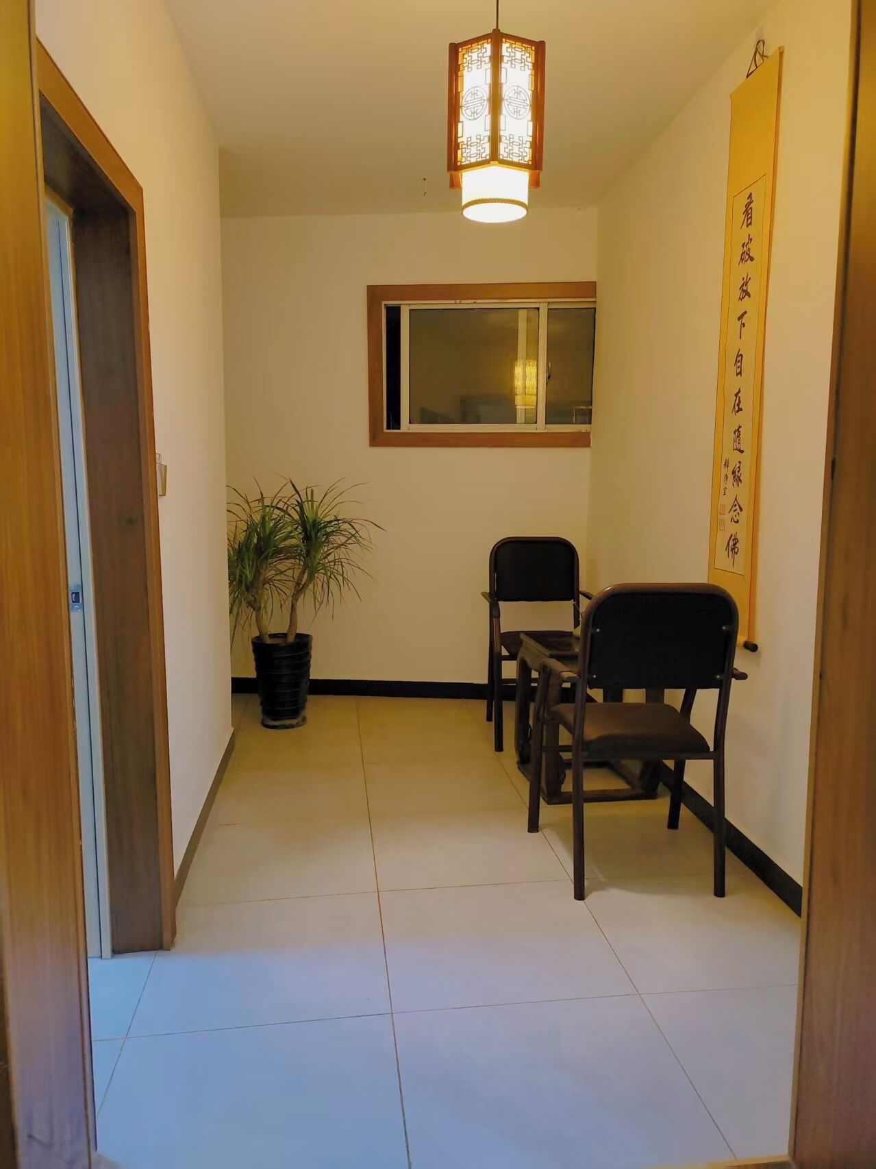 Un couloir avec une plante en pot, une table avec des chaises, une lanterne suspendue et une fenêtre donnant sur un paysage.