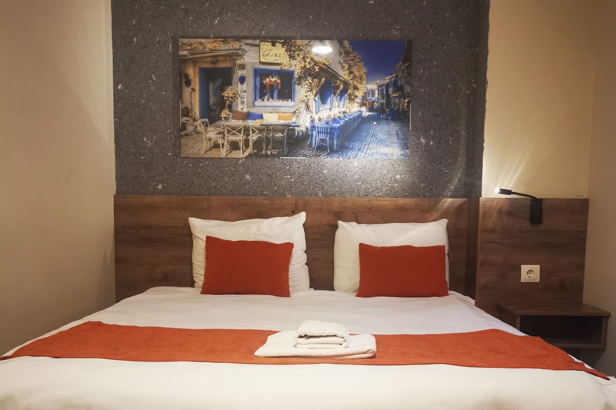 A hotel room with a large bed, a wooden headboard, a nightstand, and a wall-mounted lamp.