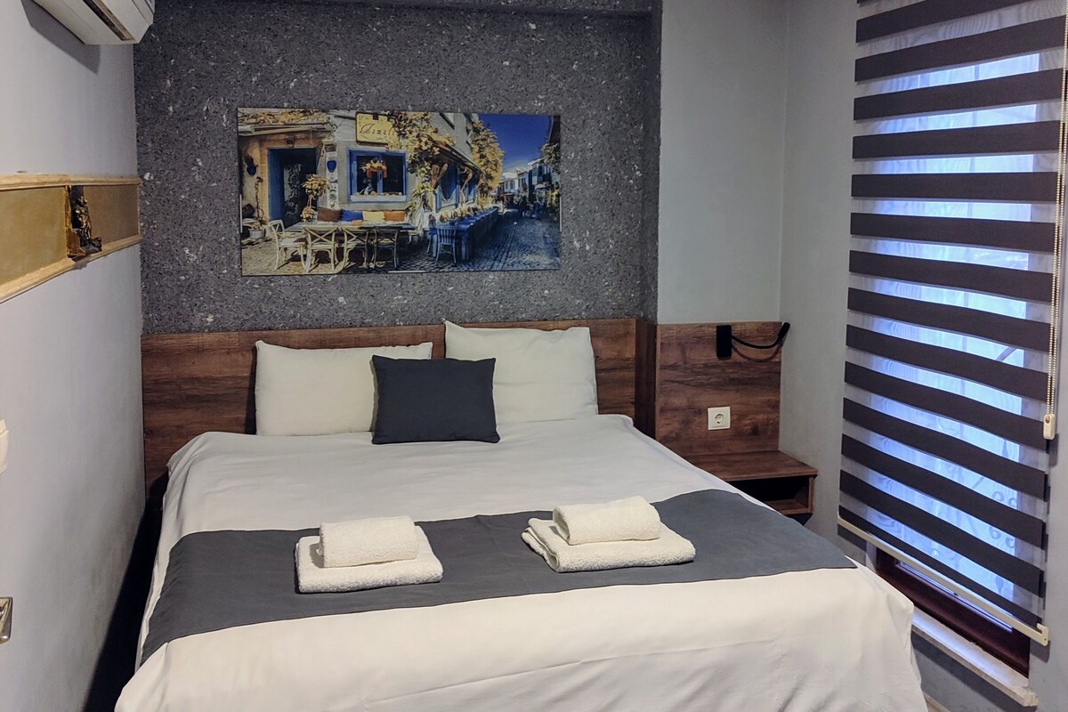A neatly made bed with a headboard, a wooden bedside table, and a wall-mounted air conditioner.