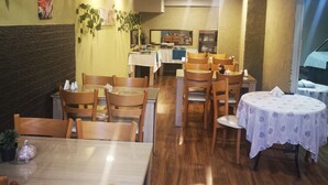 Interno di un ristorante con tavoli e sedie di legno, uno schienale piastrellato e vista della cucina sullo sfondo.
