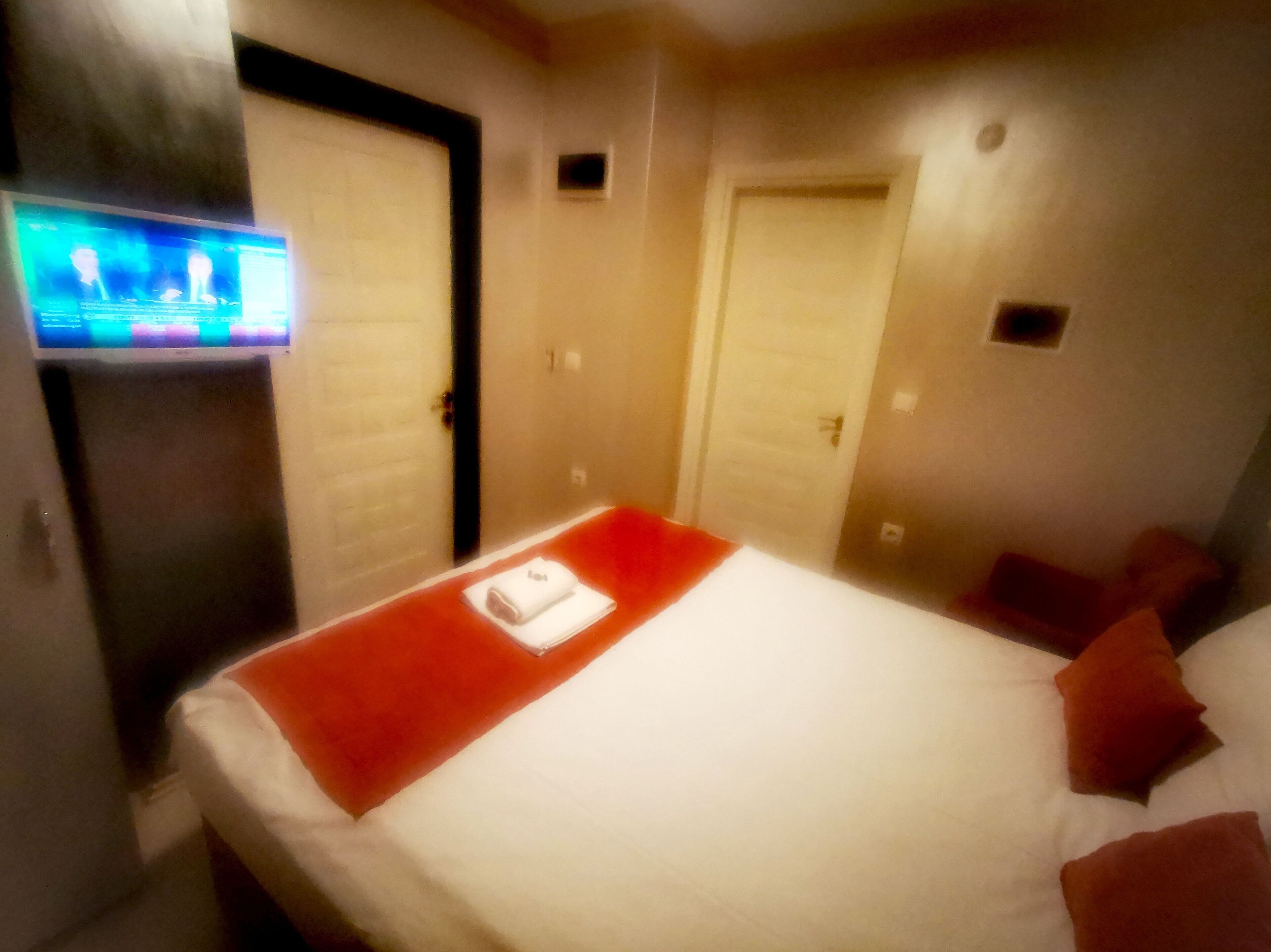 A hotel room with a bed, a TV on the wall, and two doors.