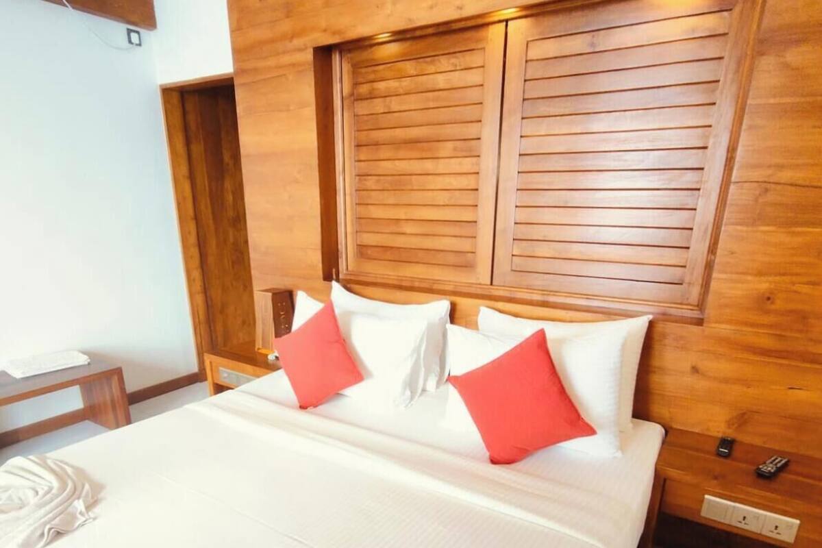 Quarto de hotel com cabeceira de madeira, cama com almofadas brancas e vermelhas, mesa de cabeceira e ar condicionado fixado na parede.