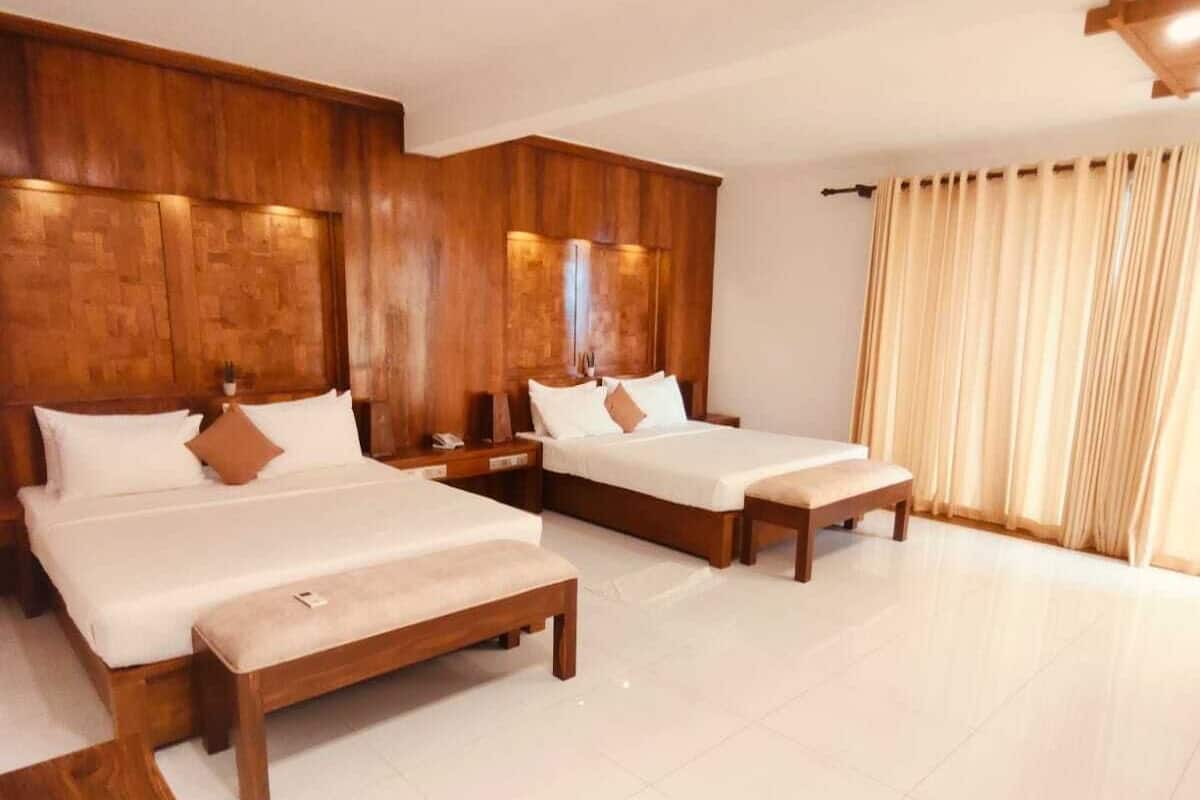 Quarto de hotel com três camas de madeira, uma janela grande com cortinas e piso ladrilhado.