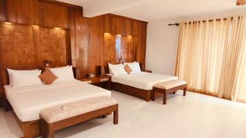 A hotel room with three wooden beds, a large window with curtains, and a tiled floor.