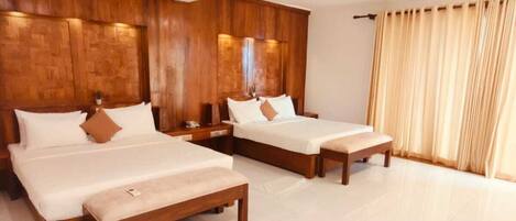 A hotel room with three wooden beds, a large window with curtains, and a tiled floor.