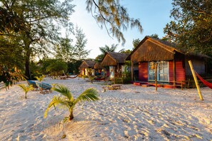 Un resort en la playa con cabañas de techo de paja, palmeras y sillas de descanso.