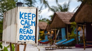 A weathered sign with the message "KEEP CALM AND READ BOOKS" in a tropical setting with thatched-roof huts and lounge chairs. - Bamboo Jam (Koh Rong Sanloem)