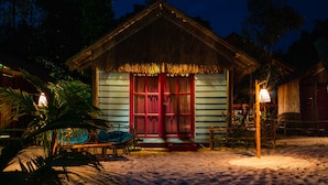A thatched-roof hut with a red door, surrounded by sand and palm trees. - Bamboo Jam (Koh Rong Sanloem)