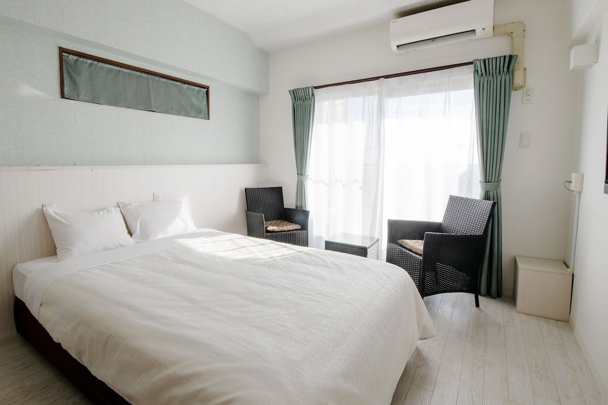 Une chambre d’hôtel avec un grand lit, une chaise, une petite table et un appareil de climatisation.