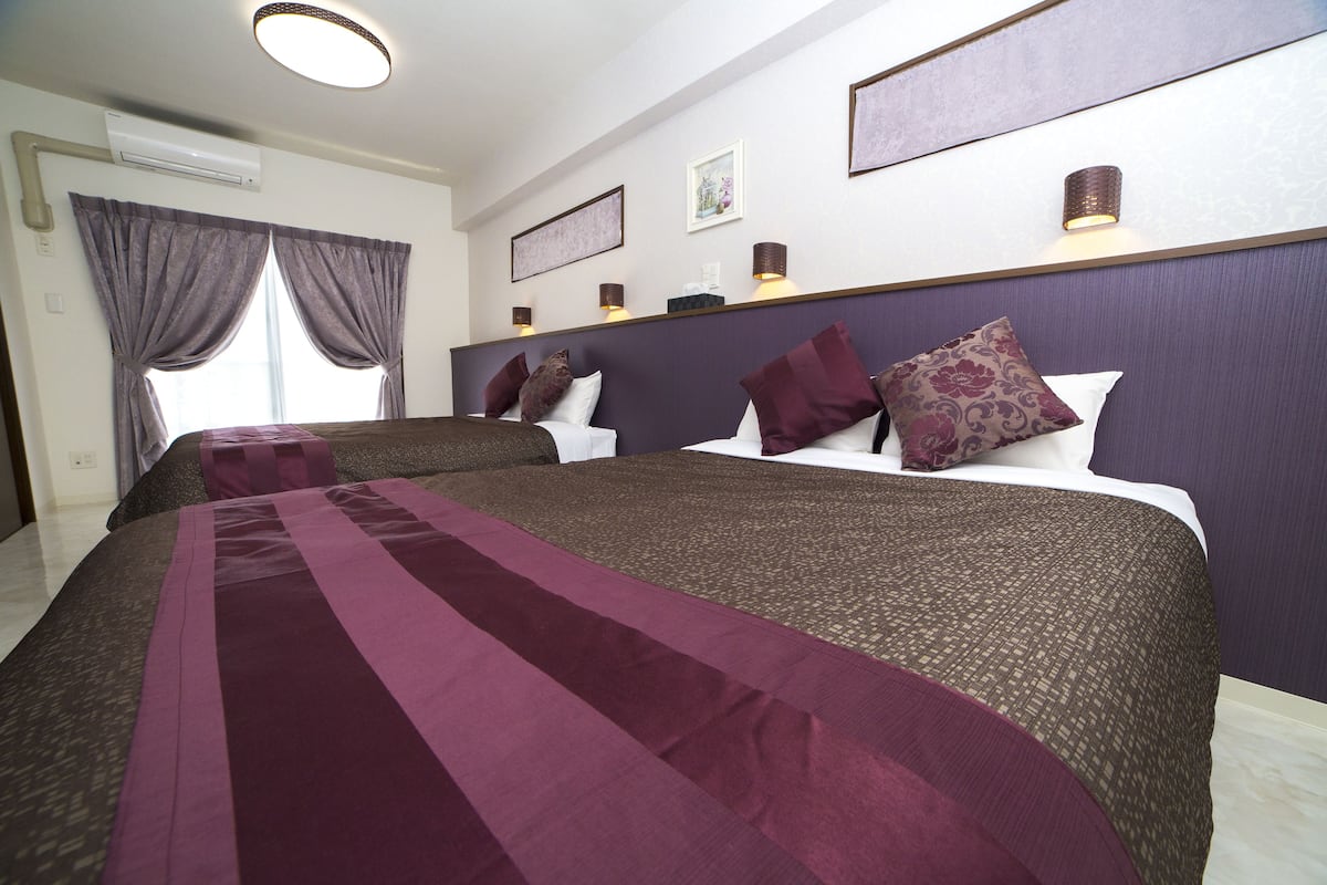Une chambre d’hôtel avec deux lits, une grande fenêtre avec des rideaux, un appareil de climatisation et des lampes fixées au mur.