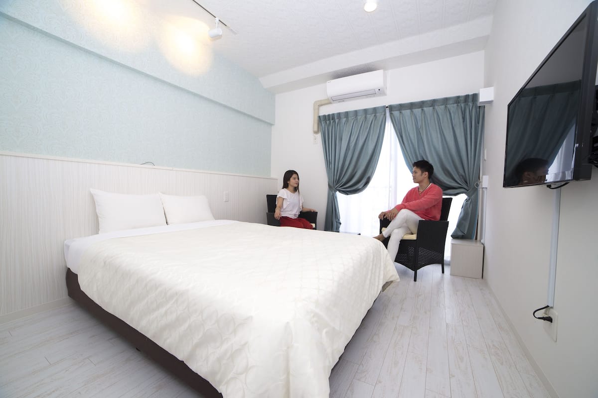 Une chambre d’hôtel avec un grand lit, un téléviseur fixé au mur et une fenêtre avec des rideaux.