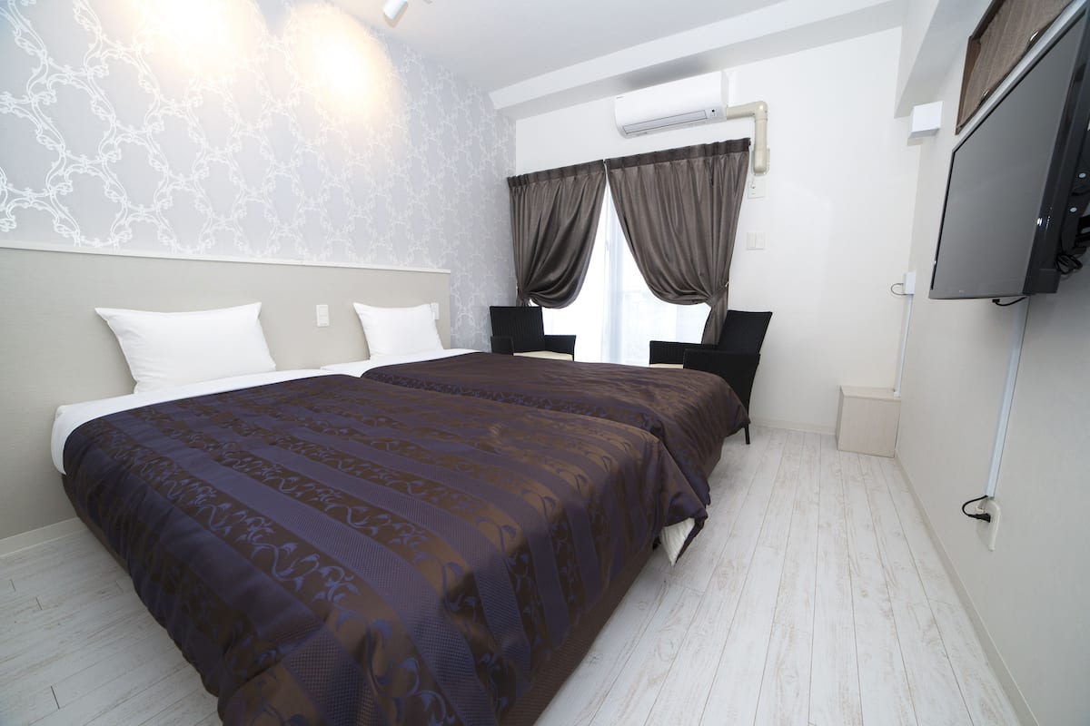 Une chambre à coucher avec un grand lit, deux tables de chevet, un téléviseur à écran plat et une fenêtre avec des rideaux.