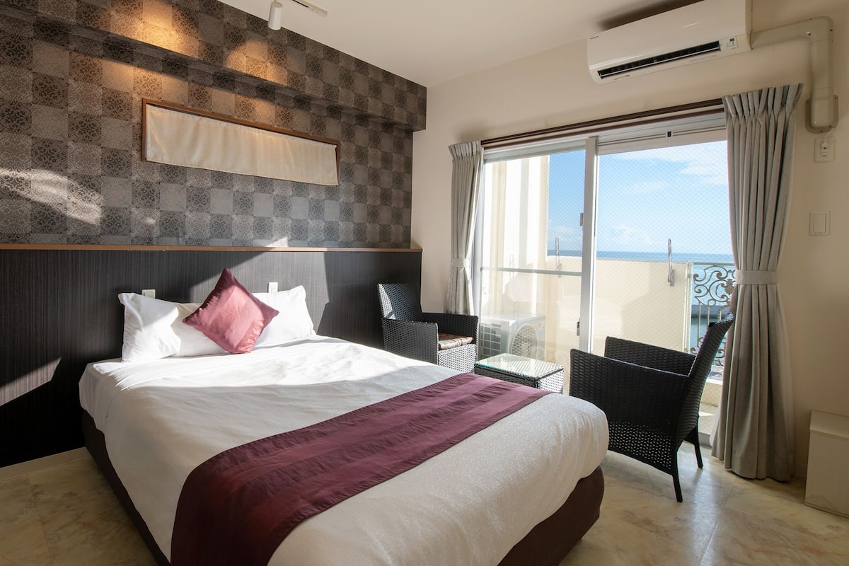 Une chambre d’hôtel avec un grand lit, une vue sur la mer et un balcon équipé d’une chaise.
