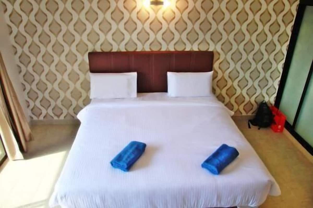 Habitación de hotel con papel tapiz estampado, cabecera de madera, ropa de cama blanca y dos toallas enrolladas sobre la cama.