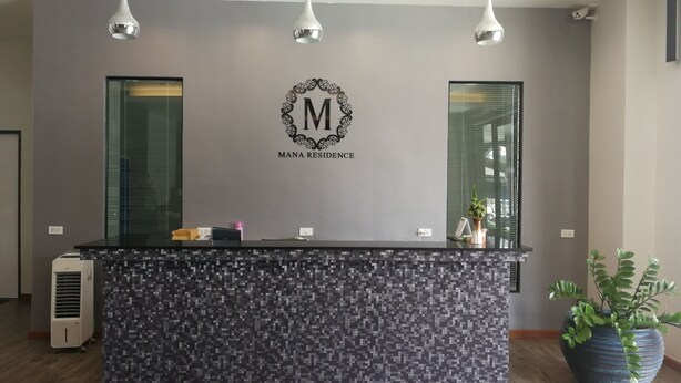 A reception desk with a logo, a potted plant, and a modern design. - Mana Residence (Hat Yai)