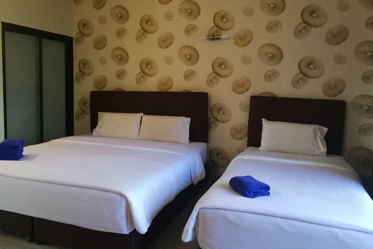 Habitación de hotel con dos camas, cada una con ropa de cama blanca y cabeceros oscuros. El papel tapiz de las paredes presenta un diseño circular.