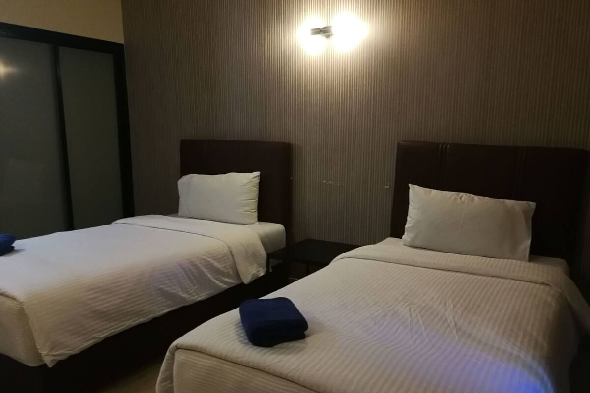 Dos camas individuales con cabeceras, una lámpara fijada a la pared y una puerta con sistema deslizante.