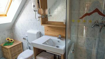A bathroom with a skylight, a toilet, a sink, a shower, and a wooden vanity.