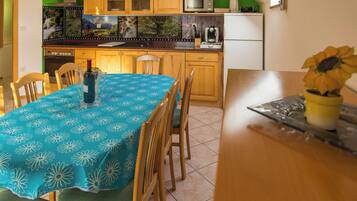 A kitchen with wooden cabinets, a microwave, and a refrigerator. There is a dining table with a blue tablecloth and chairs. A vase with a sunflower is on the table.