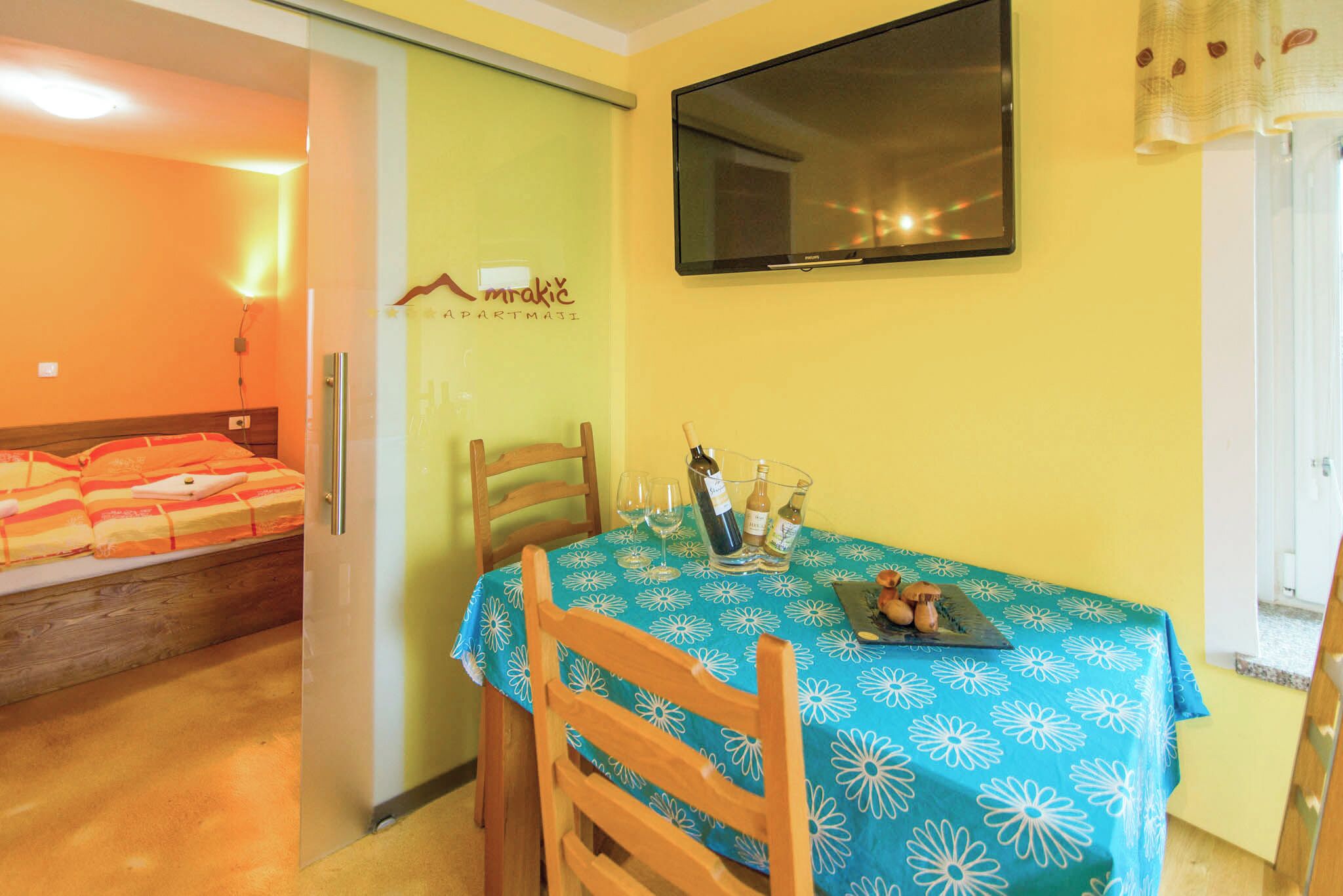 Um quarto com uma cama, uma mesa de jantar com toalha azul e uma televisão na parede.