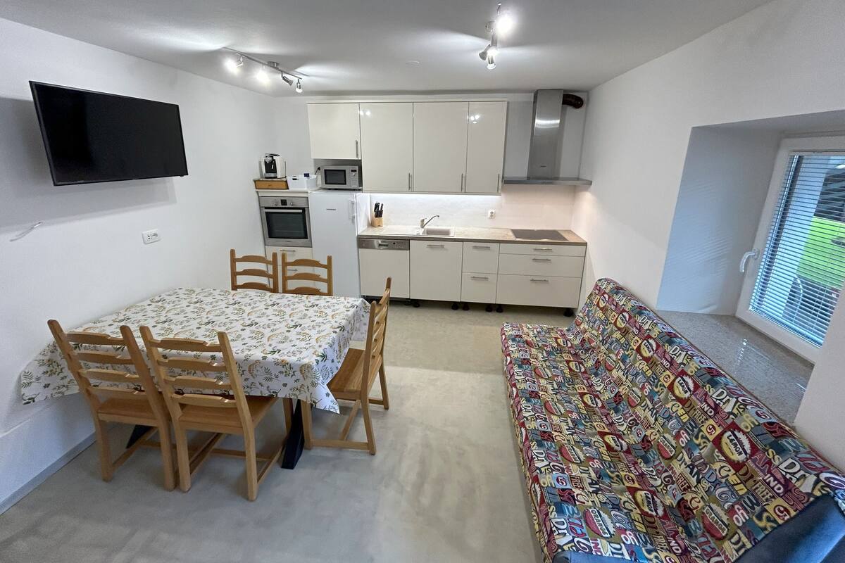 A compact kitchen with white cabinets, a microwave, and a built-in oven. There's a dining table with chairs and a bench with a colorful pattern.