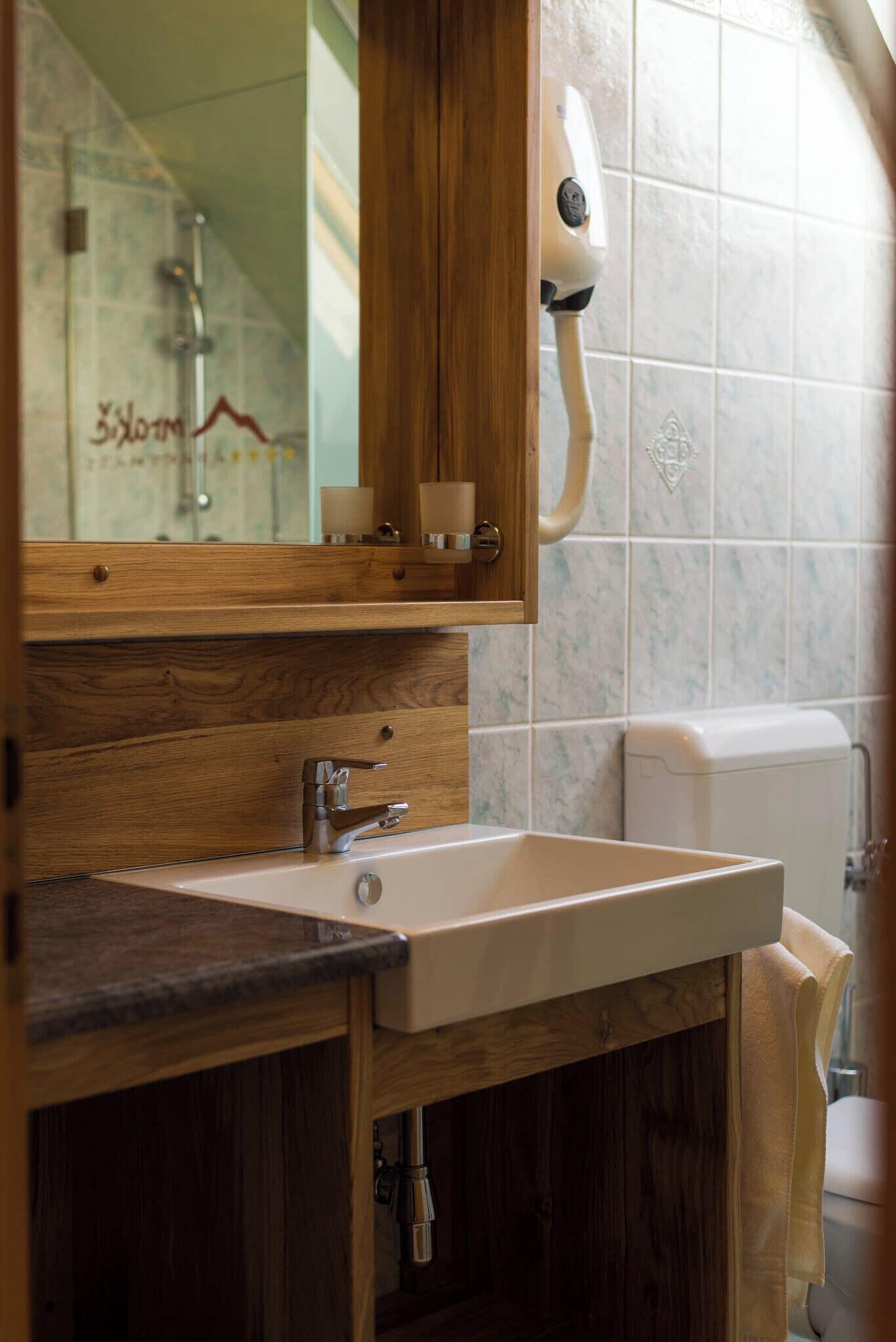 A bathroom with a wooden vanity, a white sink, a towel rack, and a hand dryer mounted on the wall.
