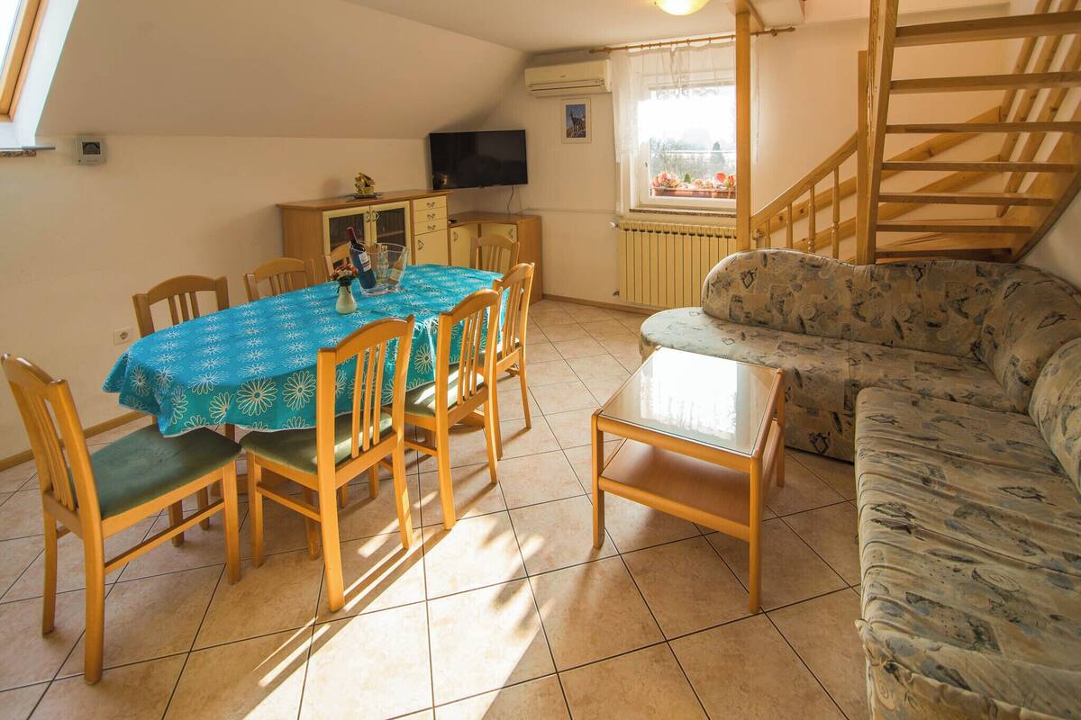 A dining area with a table and chairs, a sofa, a television, and a window with a view.