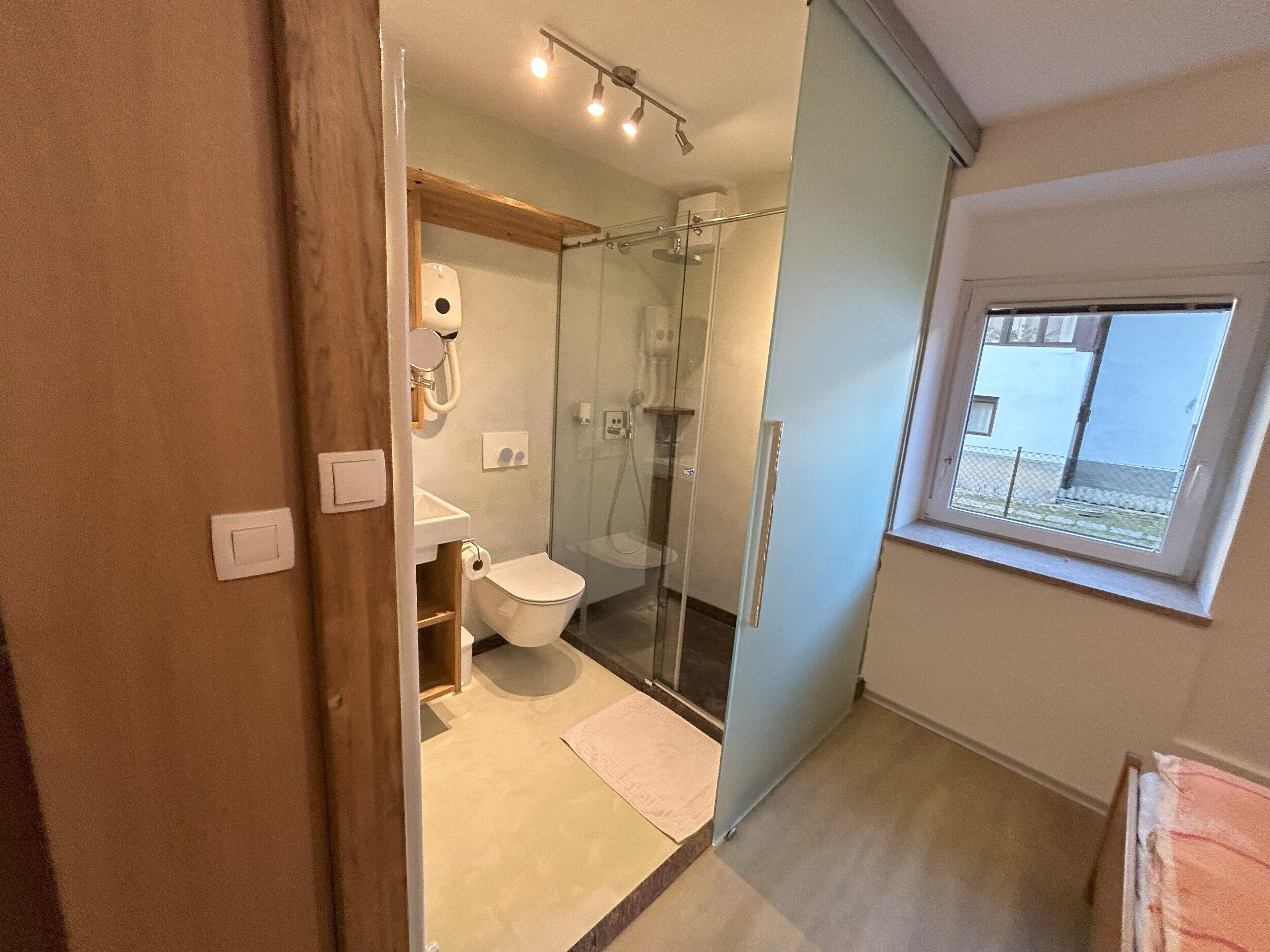 Et moderne badeværelse med glasvæg omkring bruseren, toilet og håndvask.
