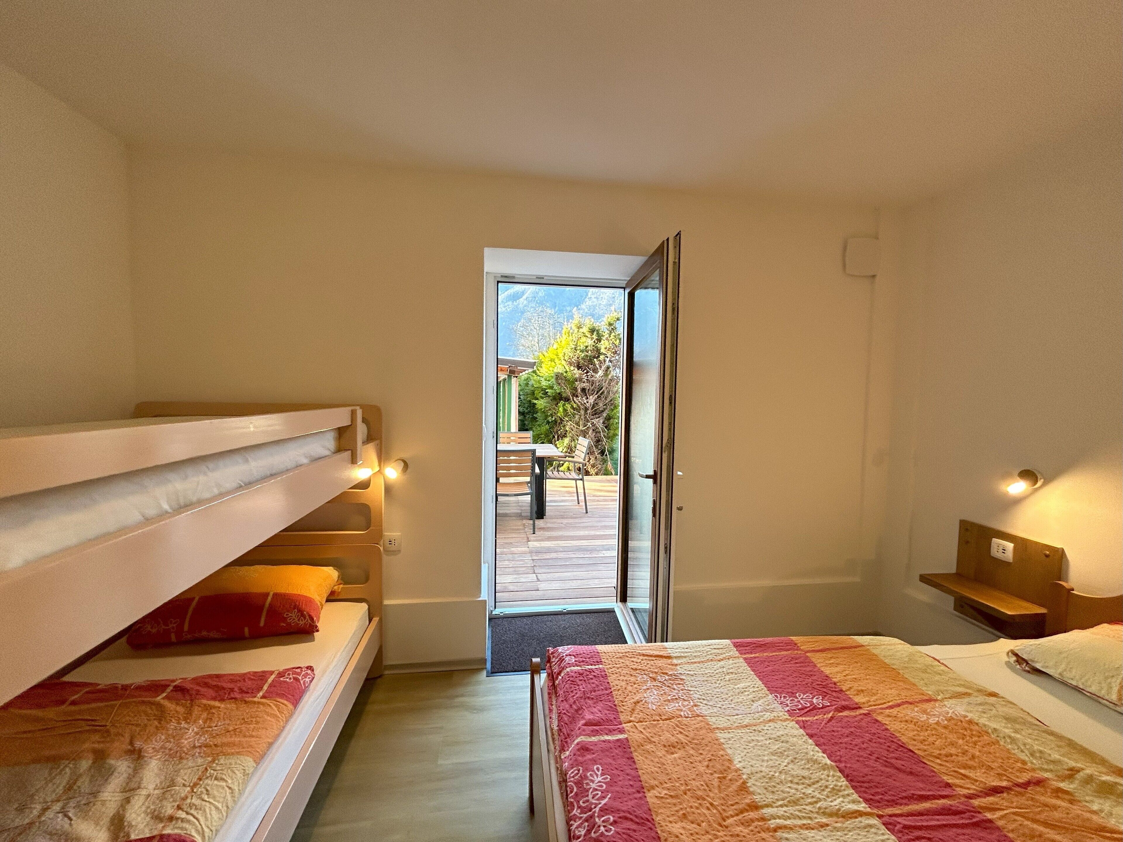 A bedroom with bunk beds, a large window, and a view of an outdoor deck.