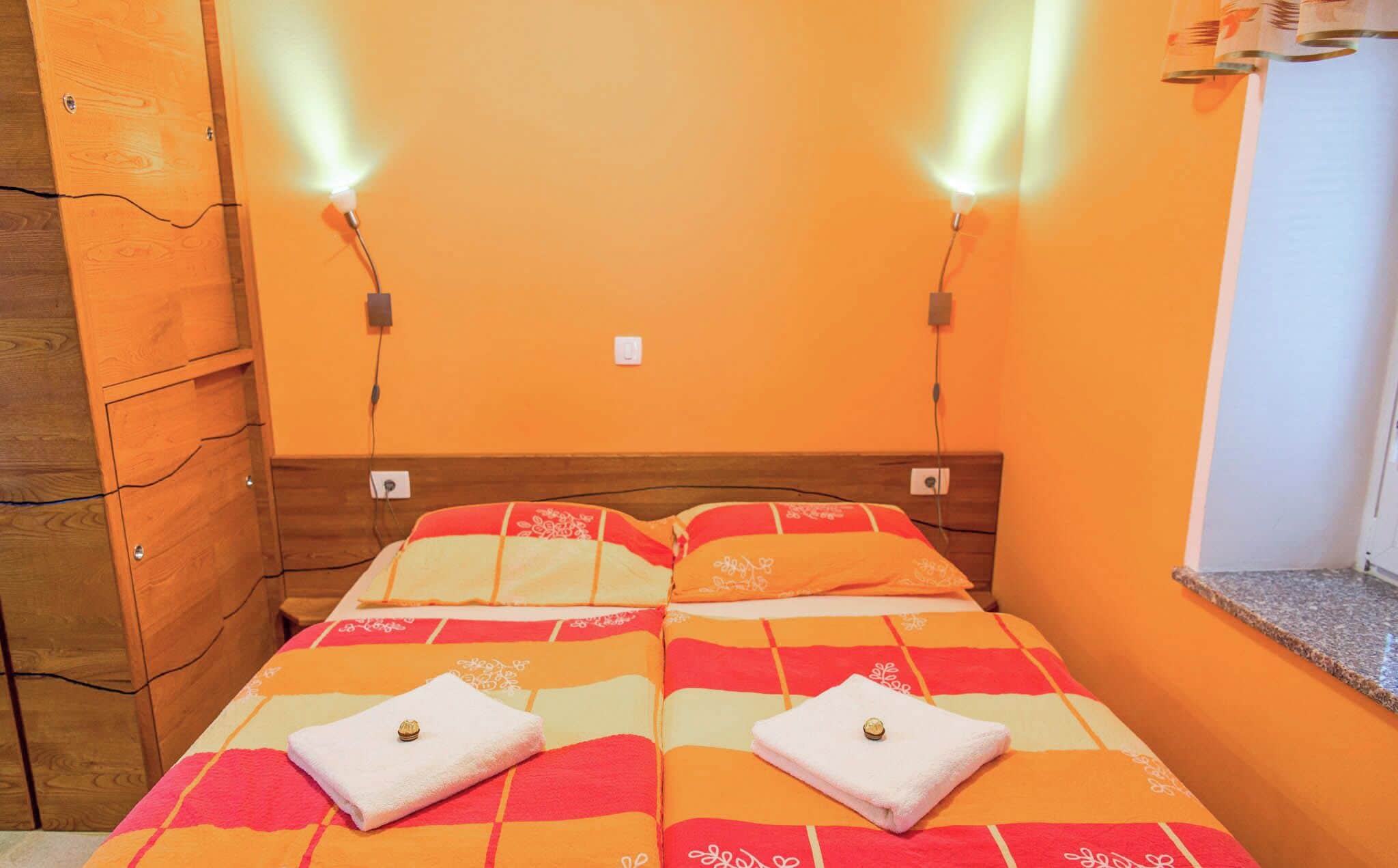 A double bed with a colorful striped bedspread, two white towels with a gold ring, and two wall-mounted lights.