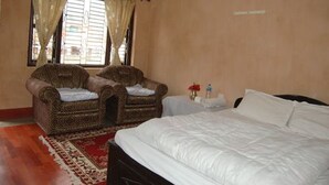 Un dormitorio con una cama grande, dos sillones tapizados, una mesita con un florero y una ventana con cortinas.