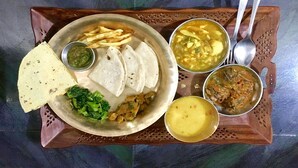 Un plato con tortillas, papas fritas, salsa verde y dos tazones de sopa, sobre una bandeja de madera.