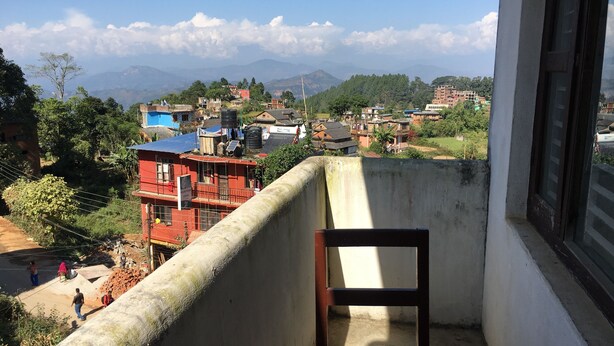 Un balcón con vista a una zona residencial, que incluye casas y montañas.