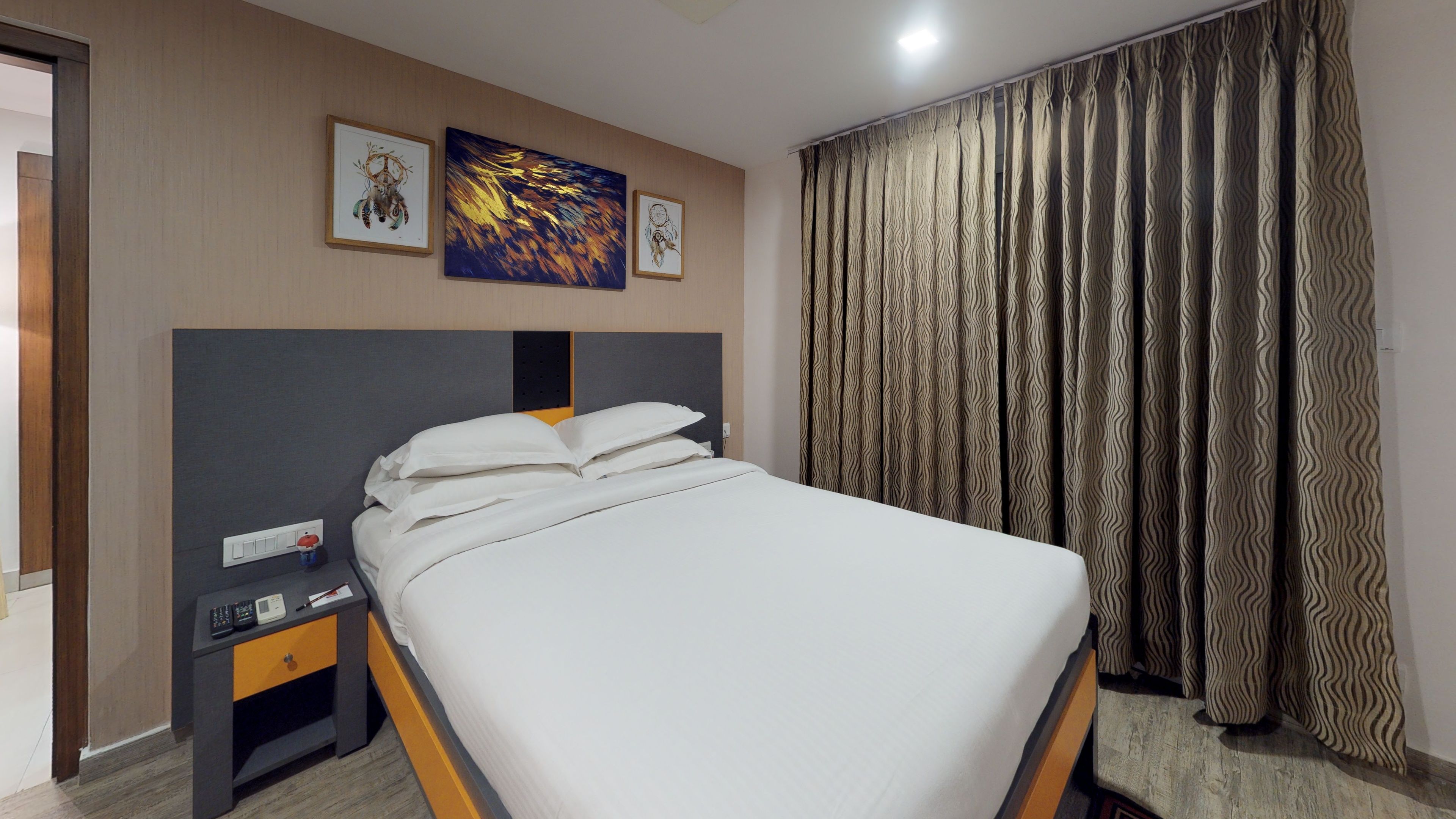A neatly made bed with white linens, a bedside table with a phone and a small lamp, and a wall with two framed artworks.