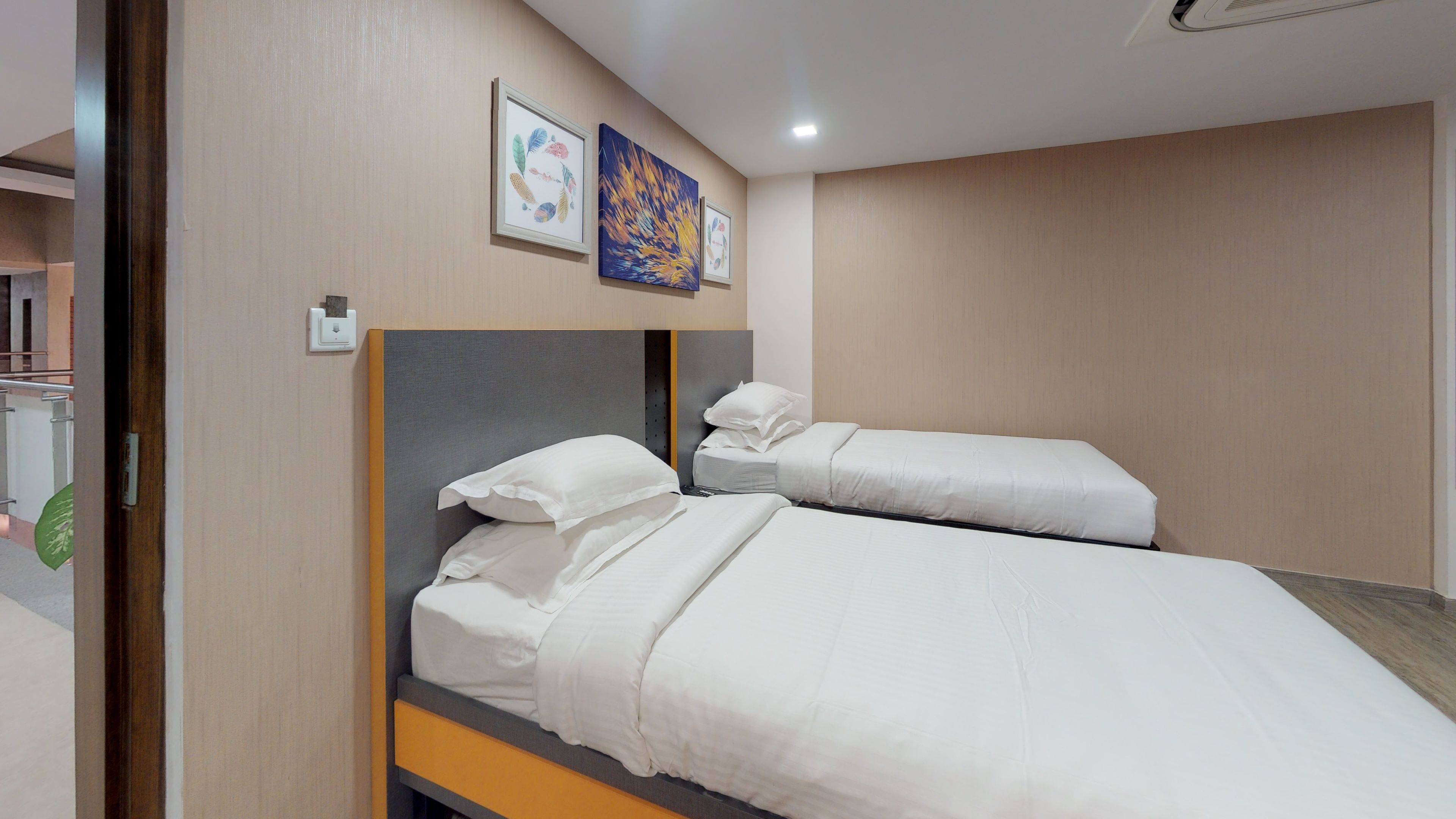 A hotel room with two beds, a wooden headboard, and two framed artworks on the wall.