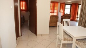 Ein Zimmer mit Esstisch und Stühlen, einem zur anderen Kammer führenden Durchgang und einem Fenster mit Vorhängen.