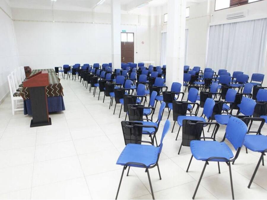 A conference room with rows of blue chairs, a podium with a black and red cover, and white walls.