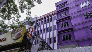 A multi-story building with a purple facade and multiple windows. There are signs for 'OYO Hotel D'Elegant' and another sign with a rooster logo.