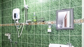 A bathroom with green marble tiles, a white sink, a handheld showerhead, a toilet paper holder, and a mirror with a decorative frame.