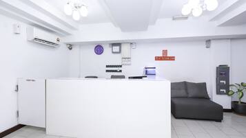 A reception area with a white reception desk, a clock, a digital display, and a grey sofa.