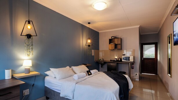 A modern hotel room with a bed, bedside table, lamp, and a small desk area.
