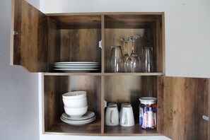 Een houten kast met planken, gevuld met borden, glazen en potten.